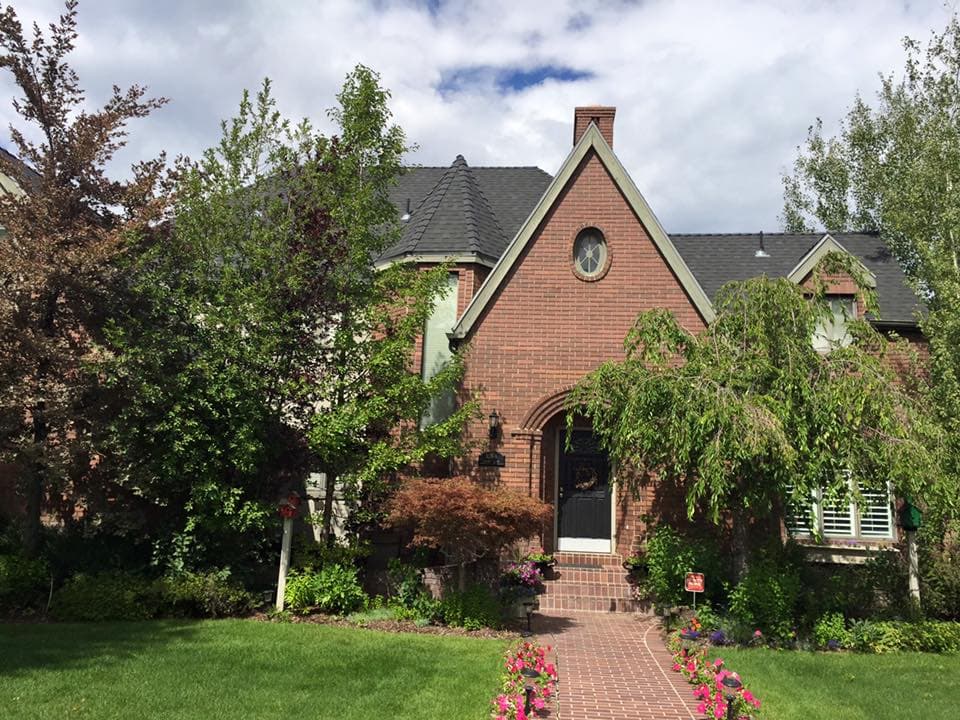 Charming brick home surrounded by lush greenery and colorful flowers in the front yard.