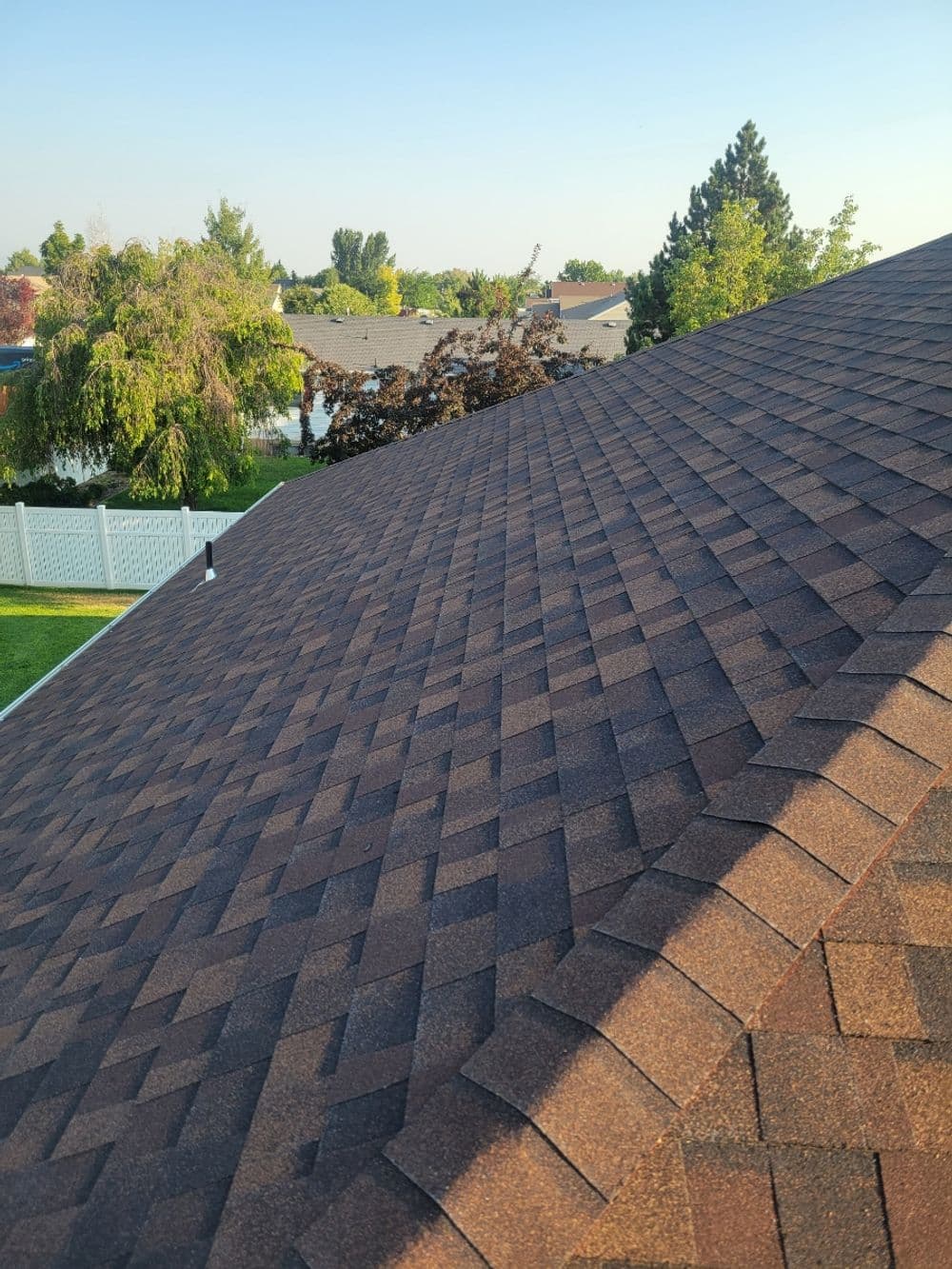 Brown shingle roof with a clear sky and trees in the background, showcasing suburban landscaping.
