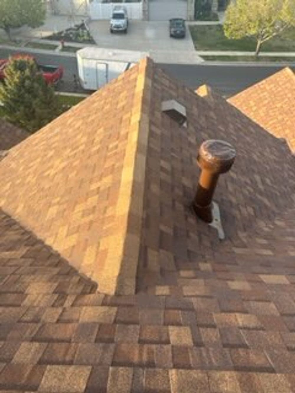 Roof shingles on a house with a chimney and nearby vehicles visible in the background.